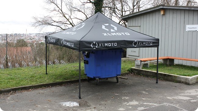 Spanngurt und Altpapiercontainer sichern das Zelt